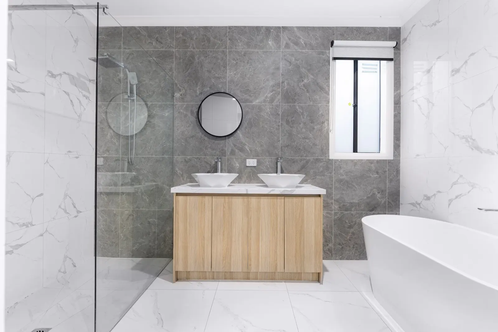 A remodeled bathroom with marble-look tile, a double vanity and a freestanding tub.