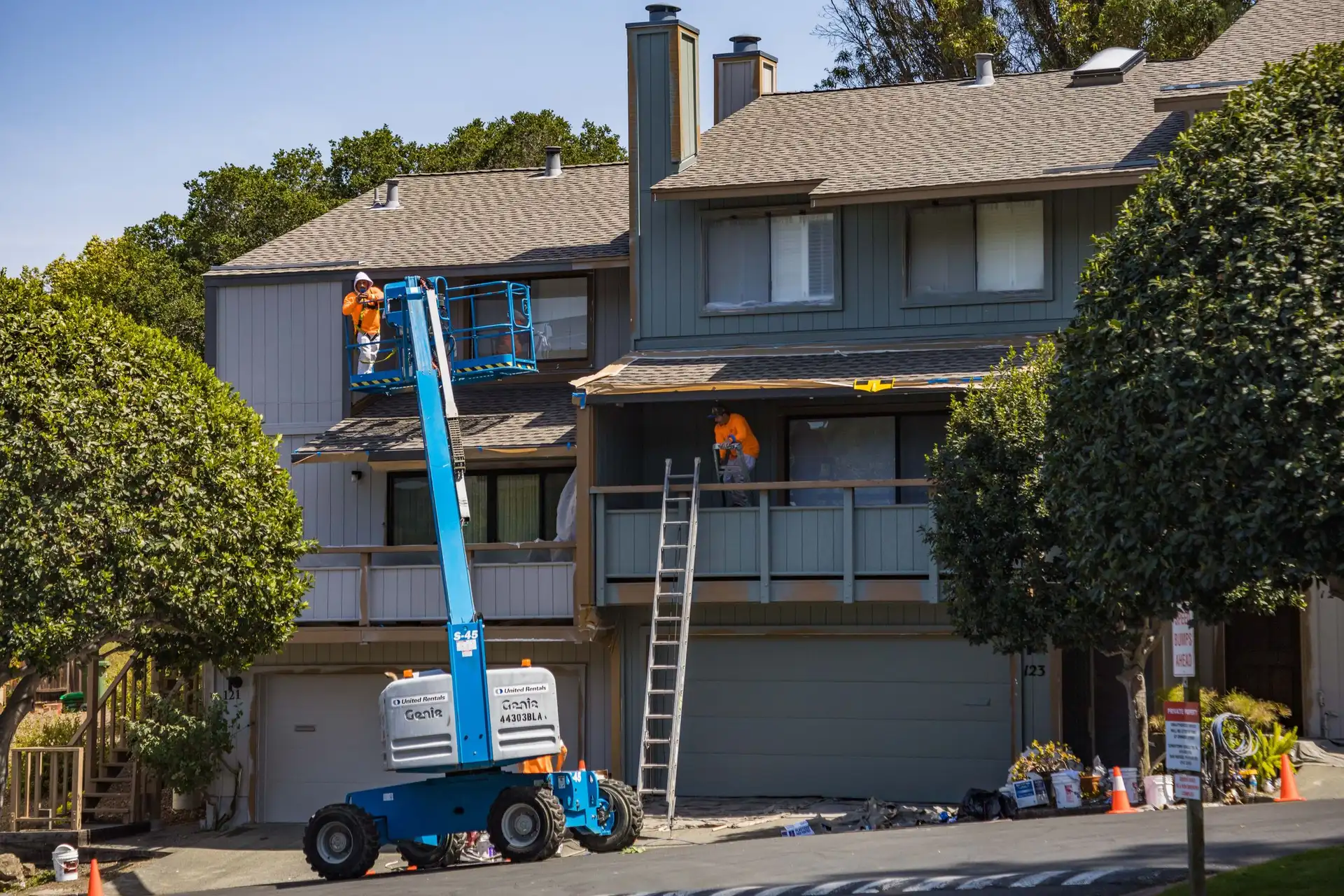 Painters working from a lift to repaint the exterior of a two-story building.