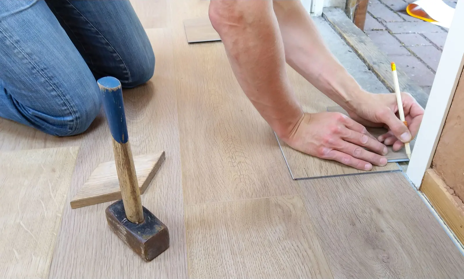 A flooring installer measuring and marking a plank before cutting it to fit.