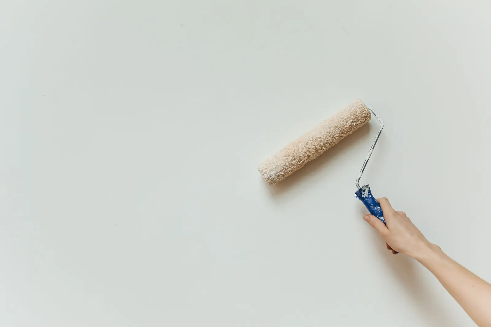 A roller loaded with white paint being rolled across a smooth interior wall.