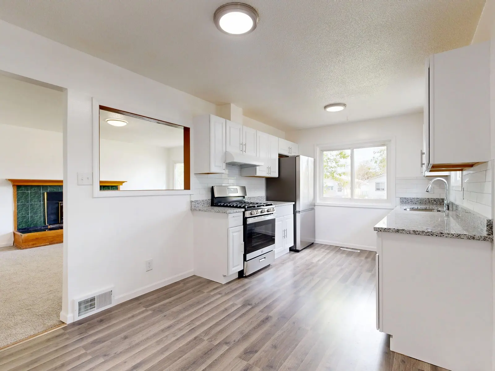 A renovated kitchen with white shaker cabinets, a stainless steel range and light plank flooring.