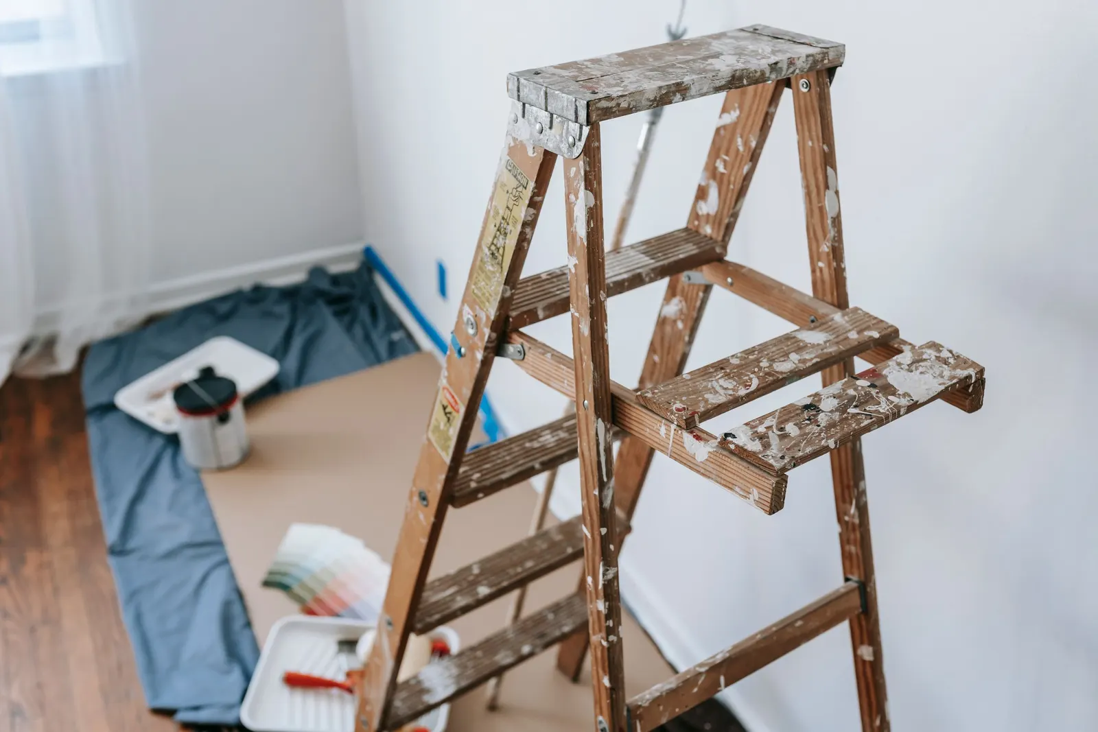 A wooden step ladder and painting supplies on a drop cloth in an empty room.