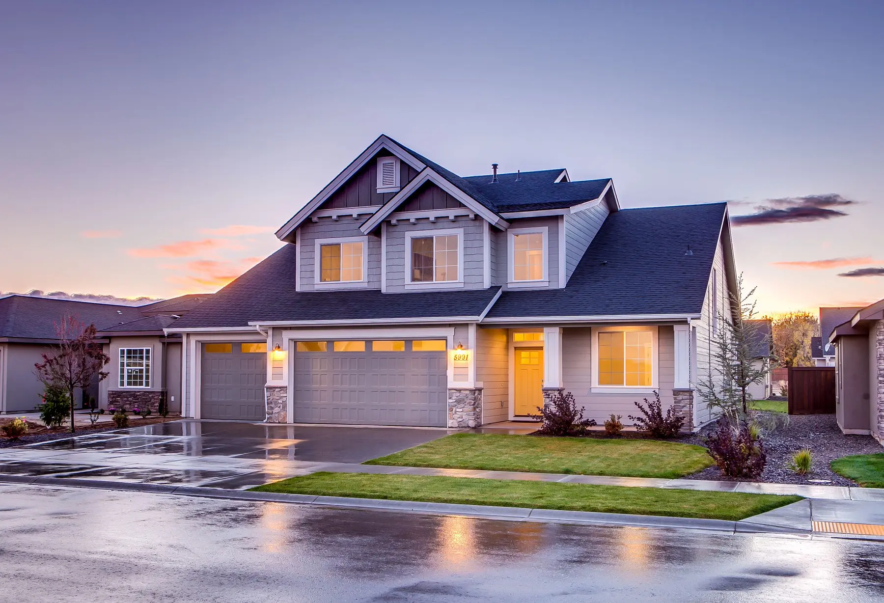 A two-story suburban home at dusk with warm light in the windows and a wide driveway.