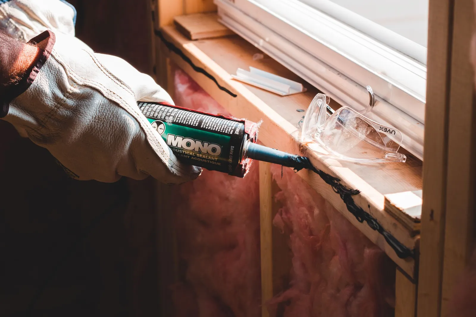 A gloved hand running a bead of caulk along the trim of a newly installed window.